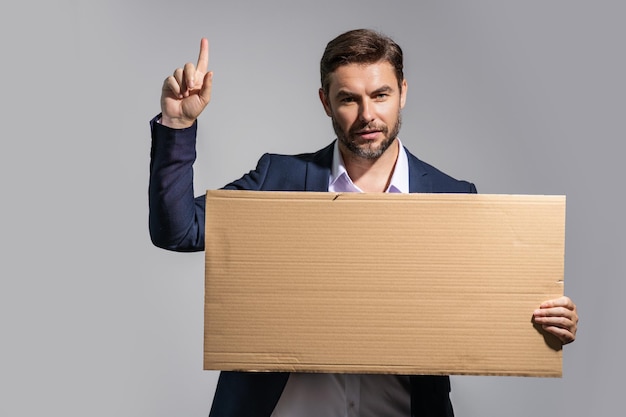 Man in suit holding empty board and pointing index finger up on studio background guy showing blank