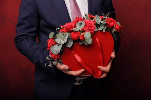 Uomo in un vestito che tiene in una mano una scatola rossa di rose