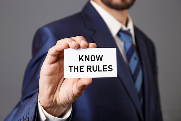 A man in a suit holds a card that says know the rules