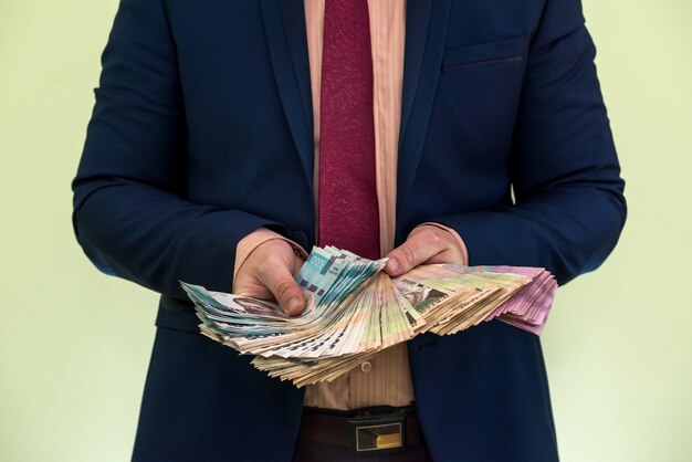 A man in a suit holds a large pile of Ukrainian money and shows his income. UAH. new banknotes 1000 and 500 hryvnia