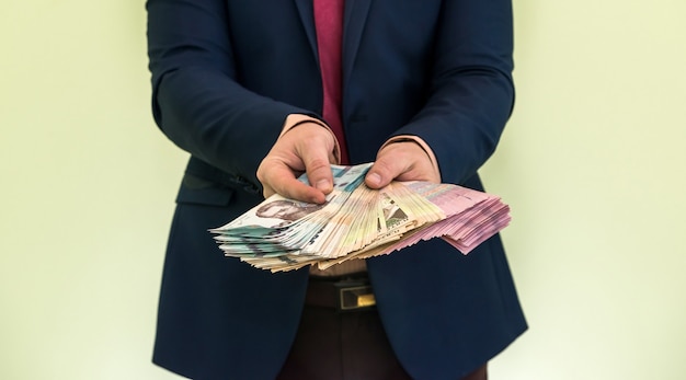 A man in a suit holds a large pile of Ukrainian money and shows his income