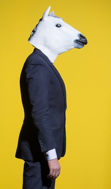 A man in a suit and a horse mask on a yellow background. Conceptual business background