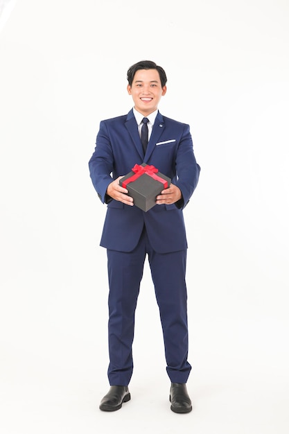 A man in a suit is holding a gift box with a red ribbon.