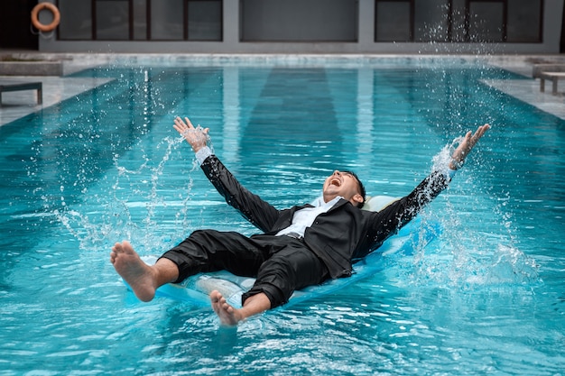 A man in a suit is resting in the pool on an inflatable blue mattress
