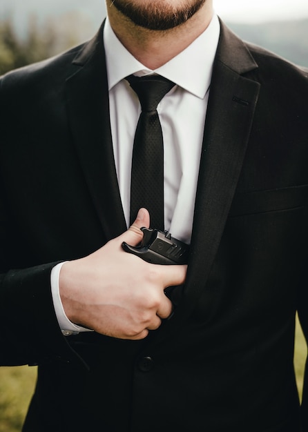 A man in a suit, jacket and white shirt, black tie, holding a gun in his hand.