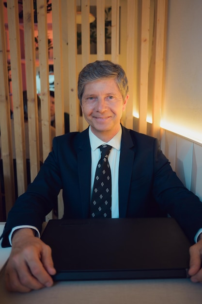 Man in suit sitting at table with laptop looking at camera in a coffee shop