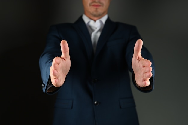 A man in a suit spreads his arms to the side on black