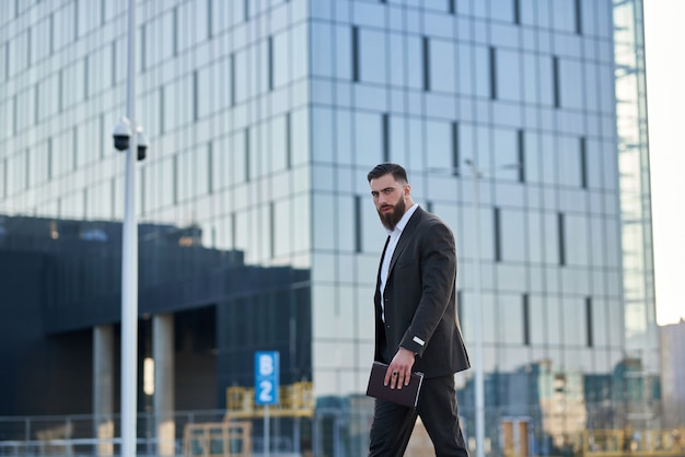 Man in suit standing in front skyscrapers calling with him work in office. Young businessman caucasian.