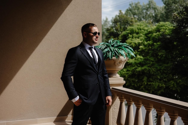 a man in a suit stands on a balcony in front of a potted plant