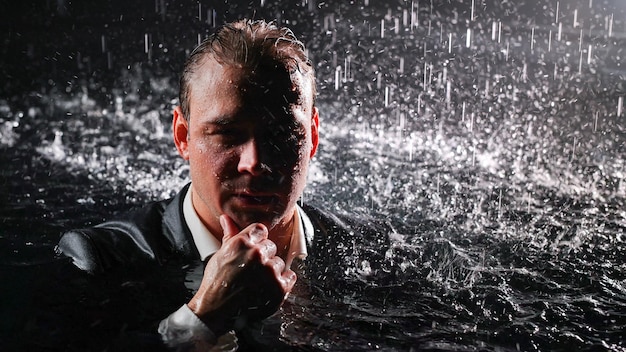 A man in a suit stands in the water in the rain and looks at the camera