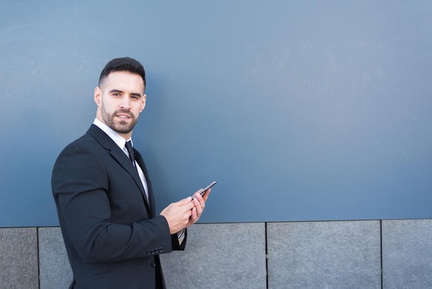 Man in suit at street messaging in smartphone and smiling looking at camera