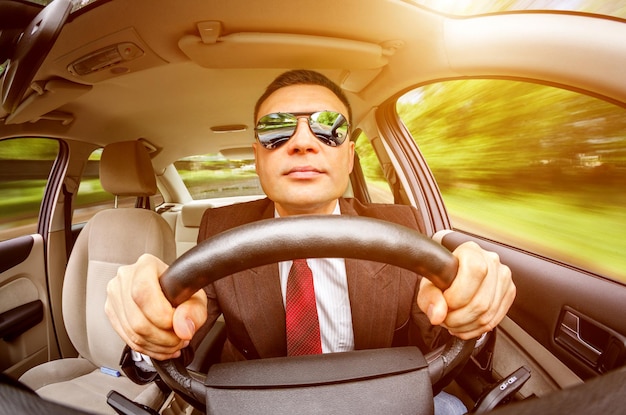 Man in a suit and sunglasses driving on a road in the car.