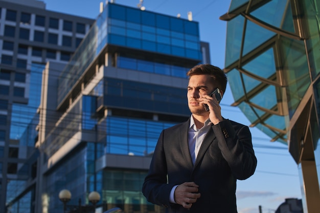 ガラスのファサードを持つ建物に対して携帯電話で話しているスーツの男
