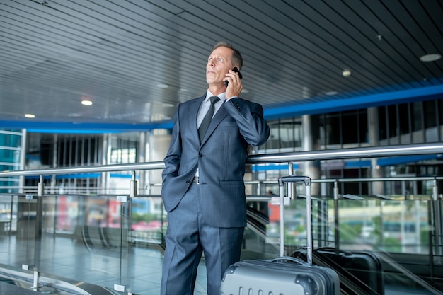 Человек в костюме разговаривает по смартфону в аэропорту