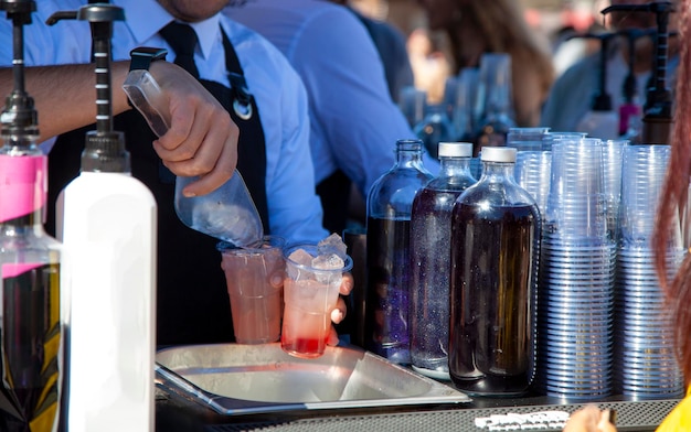 Photo man in suit, white shirt and black apron throwing ice at plastic fruit cocktails. bartender drink.