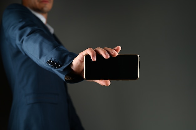 A man in a suit with outstretched hand holds a phone