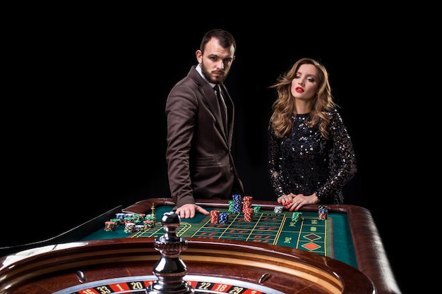 カジノでルーレットをしている美しい黒いドレスを着た女性とスーツを着た男性。ギャンブル。カジノ。ルーレット。ポーカー。