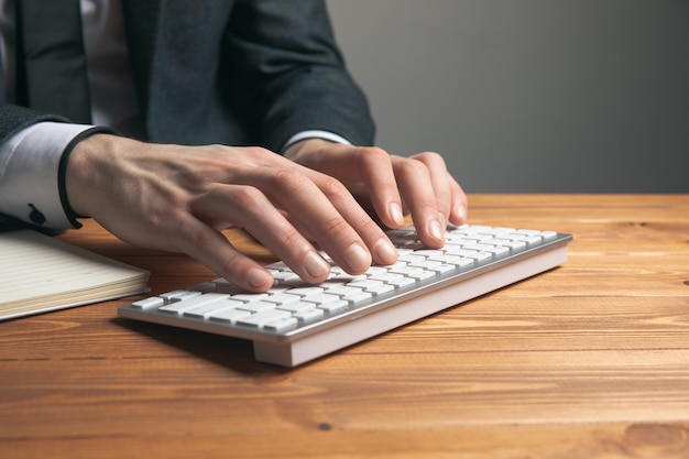 A man in a suit writes on a keyboard on a gray surface