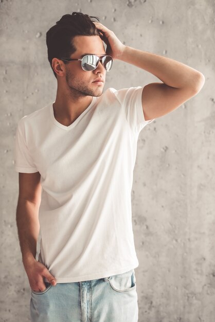 Man in sun glasses is smoothing hair and looking away.