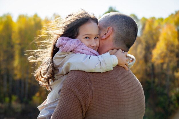 Man in sunglasses hugs beautiful daughter on background of colorful autumn trees