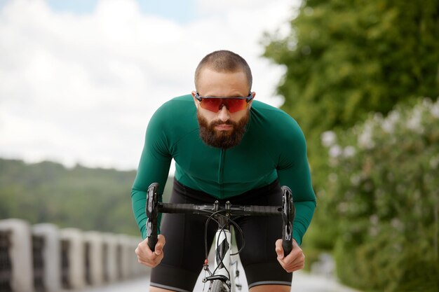 Photo man in sunglasses speeds along the road against a background of summer park man with a bicycle hobby rides in the park