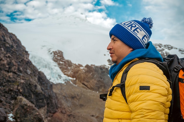 A man in and sunglasses with a backpack stands in front of a glacier in cayambe ecuador