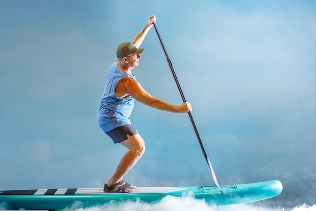 A man on a SUP board with an oar rows in the fog against the background of clouds