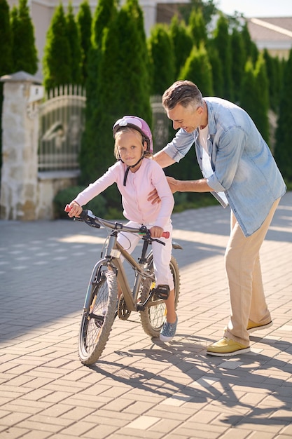 A man supporting a girl while she riding a bike