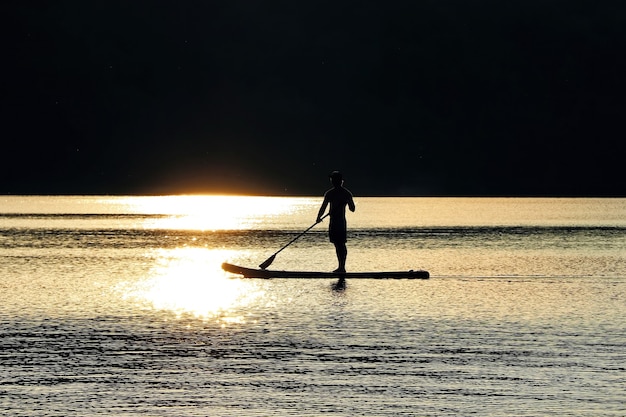 Man on a surfboard floats on water in the sunset