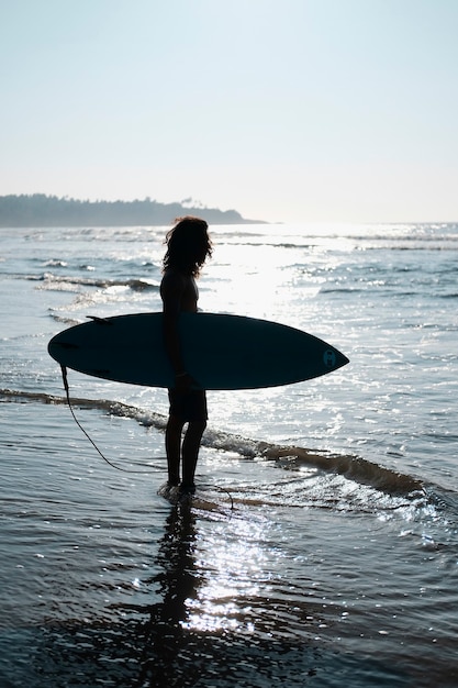 Surfista dell'uomo che si siede alla tavola da surf sulla spiaggia di sabbia