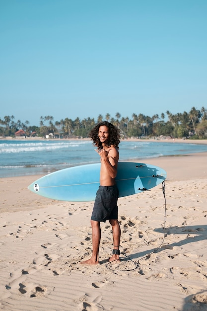 Surfista dell'uomo che si siede alla tavola da surf sulla spiaggia di sabbia