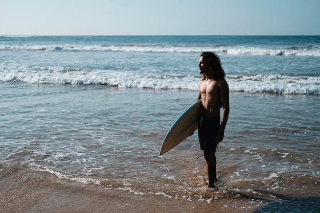 Человек-серфер сидит за доской для серфинга на песчаном пляже