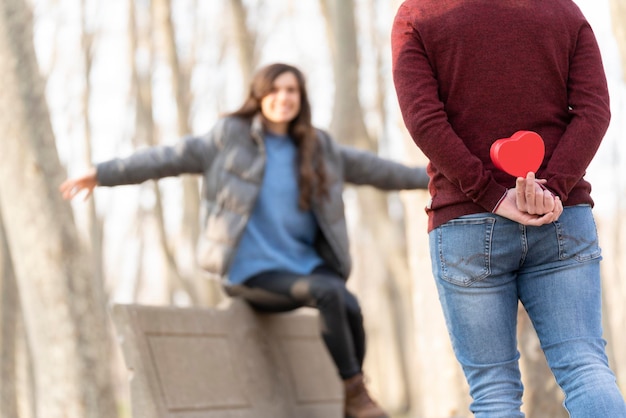 L'uomo sorprende la sua ragazza con un regalo a forma di cuore lei è seduta su una panchina nel parco