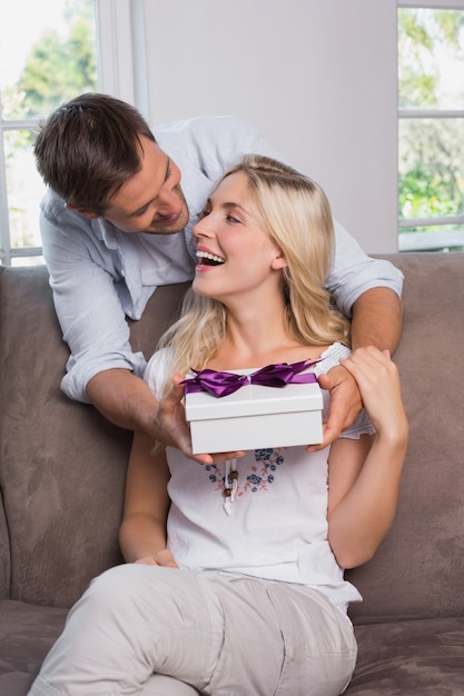 Man surprising cheerful woman with a gift at home