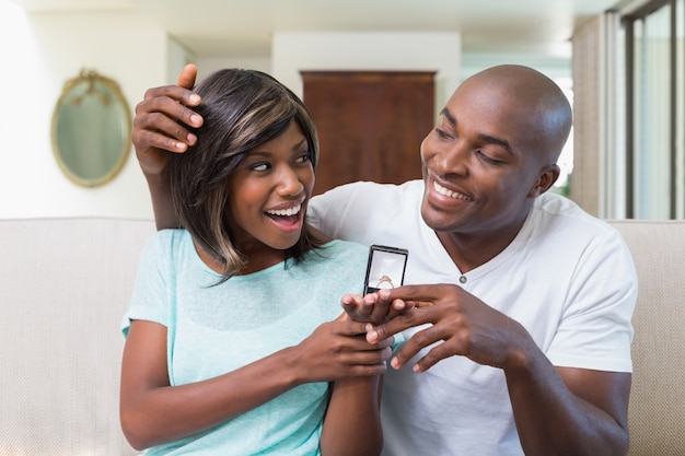 Man surprising his girlfriend with an engagement ring on the couch