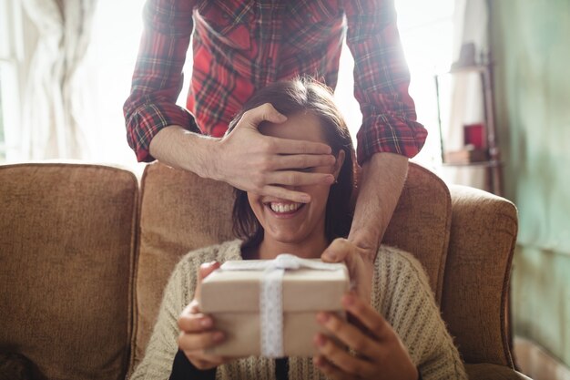 Man surprising woman with a gift in living room