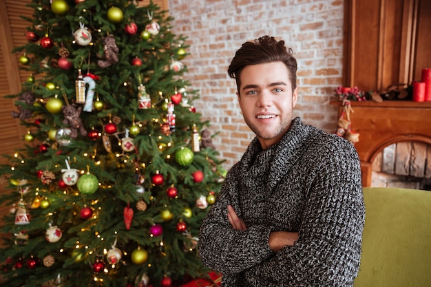 Man in sweater near the fir-tree and sofa arms crossed