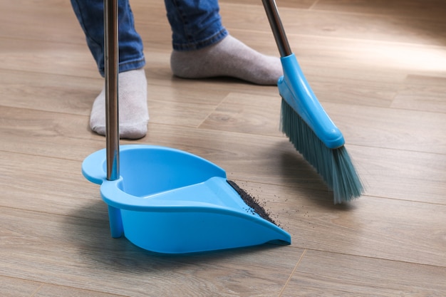 The man sweeps the debris into a blue scoop with a brush.