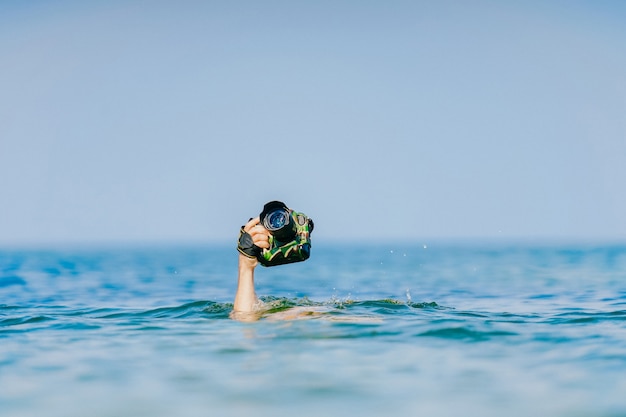 Человек плавает под водой и держит руку с фотоаппаратом