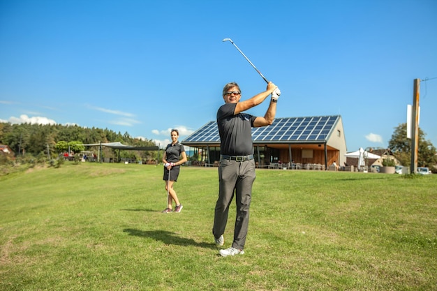 Man swinging a golf club on a golf course on a bright day