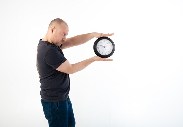 A man in a T-shirt holds a large clock