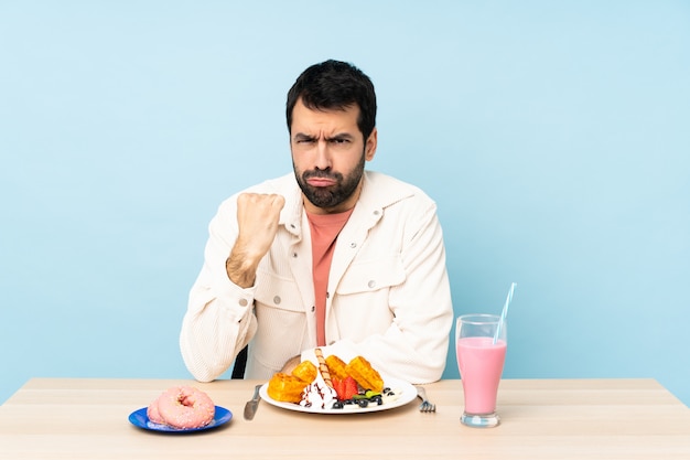 朝食のワッフルと怒っているジェスチャーでミルクセーキを持つテーブルで男