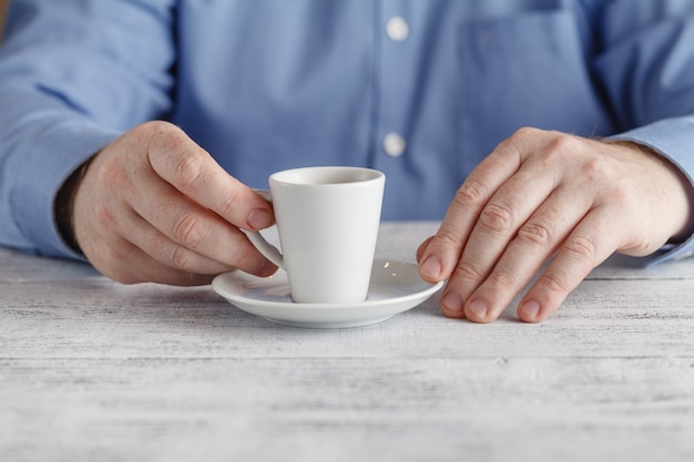 テーブルで男が彼の手でエスプレッソコーヒーのカップを保持しています。