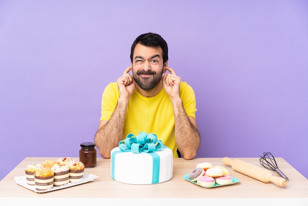 Man in a table with a big cake frustrated and covering ears