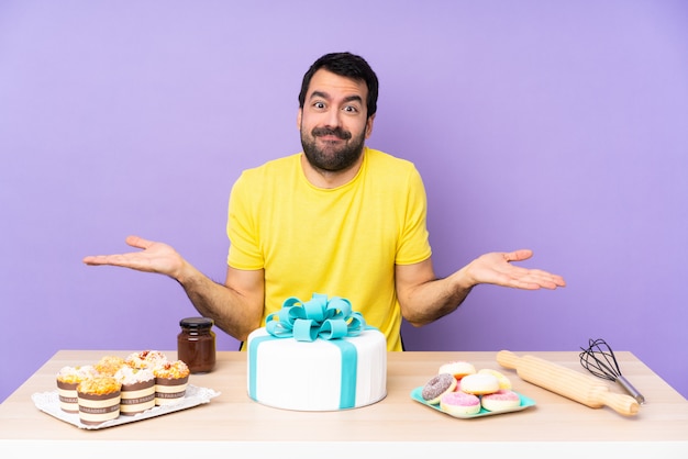 Uomo in una tabella con una grande torta che ha dubbi mentre alzando le mani