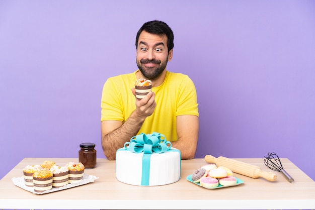 Man in a table with a big cake over purple backgroun