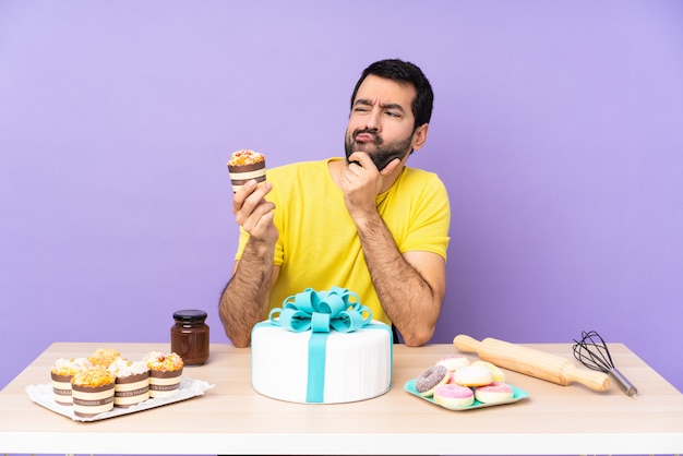 Man in a table with a big cake over purple wall