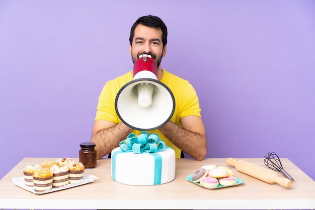 Man in a table with a big cake shouting through a megaphone