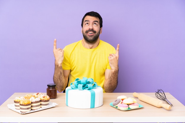 Man in a table with a big cake surprised and pointing up