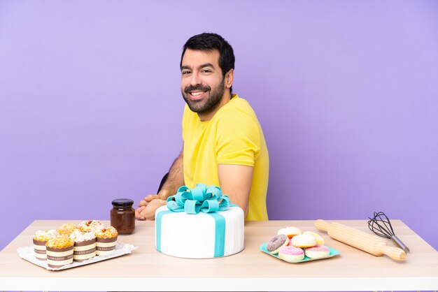 Uomo in un tavolo con una grande torta con le braccia incrociate e guardando avanti